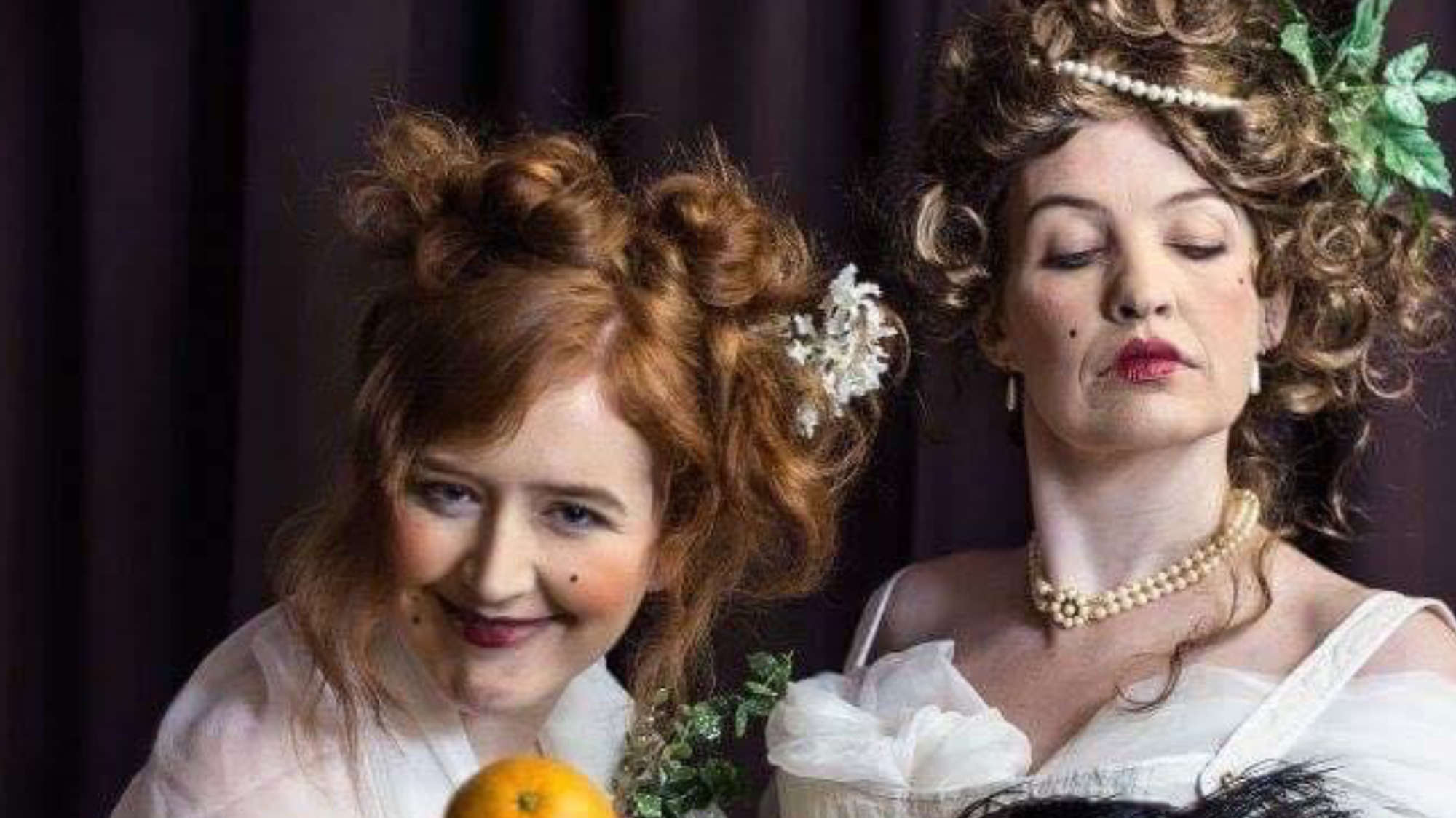 Two women with an orange and a fan